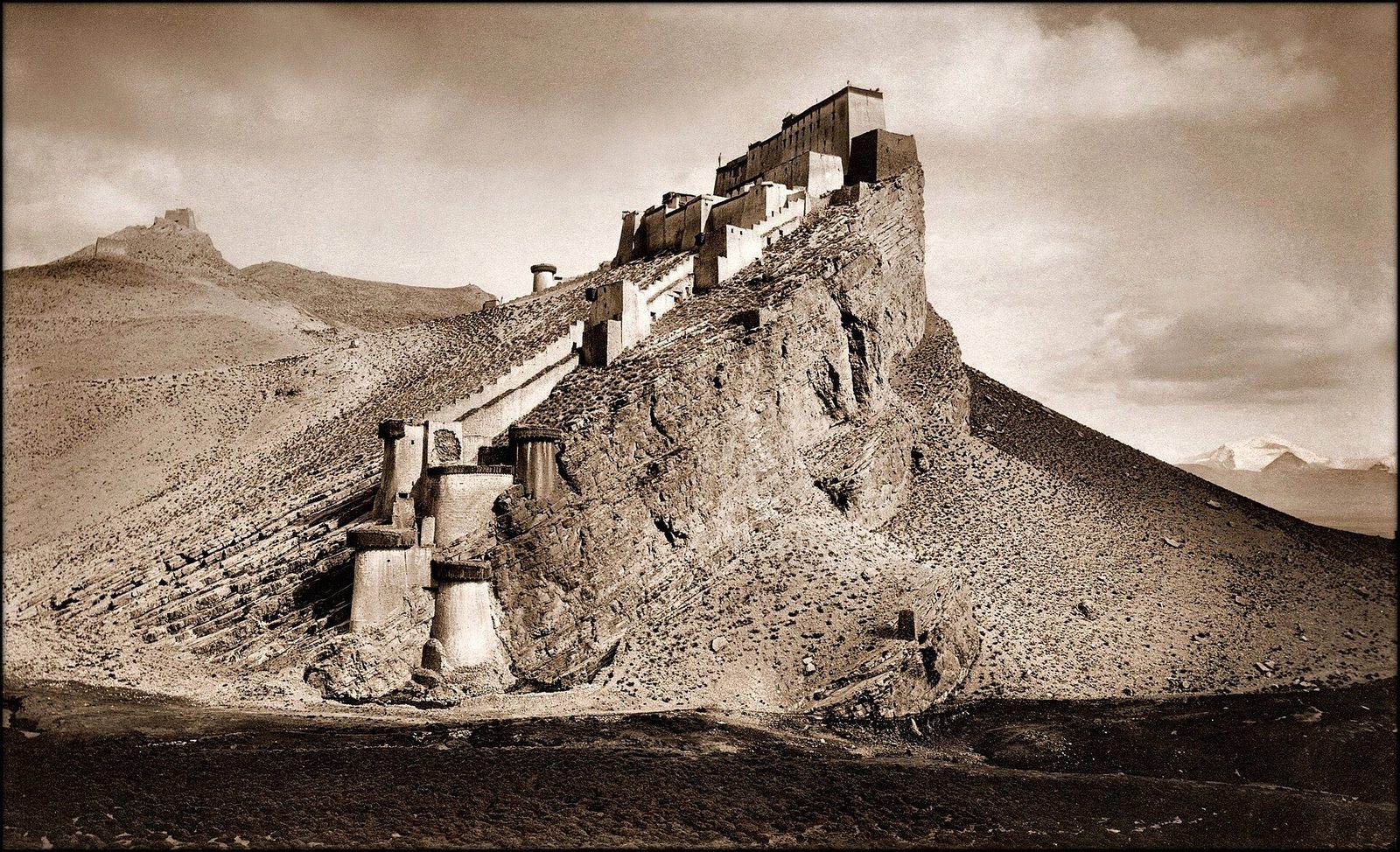 A sepia photograph of a fort with long walls running up a steep rocky ridge.