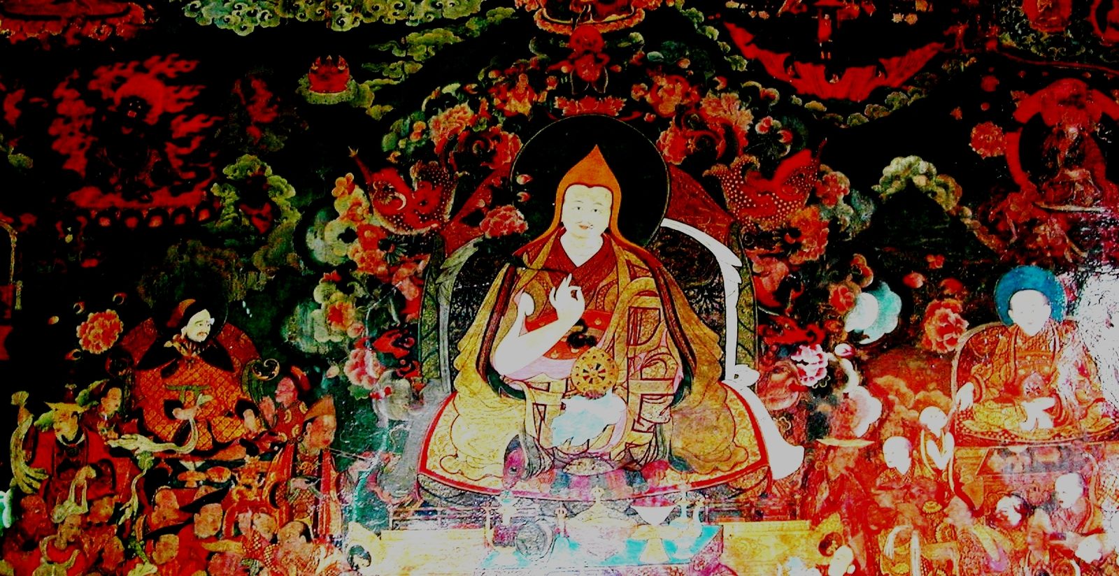 A wall painting of a seated lama in yellow robes between two figures, surrounded by smaller deities.