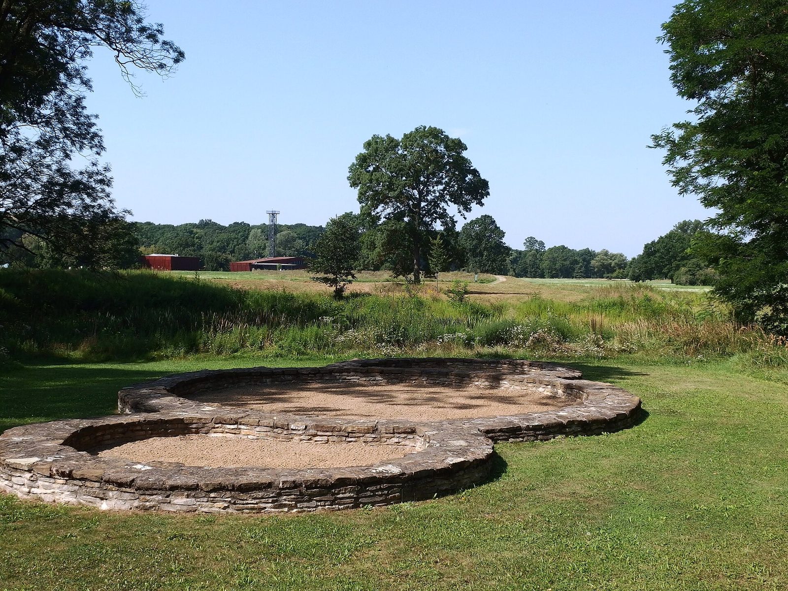 The low reconstructed foundations of a small round church with apses in a meadow.