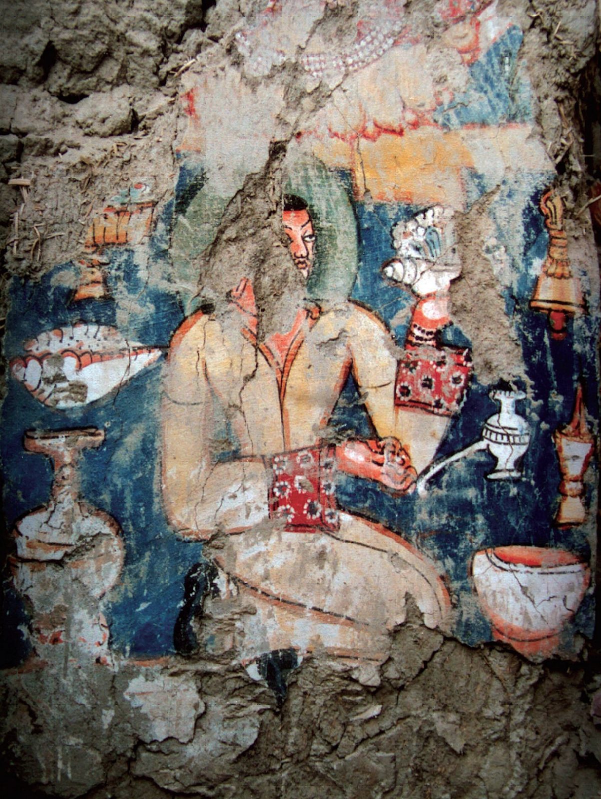 A damaged wall painting of a seated royal figure in a patterned robe, offerings around him.