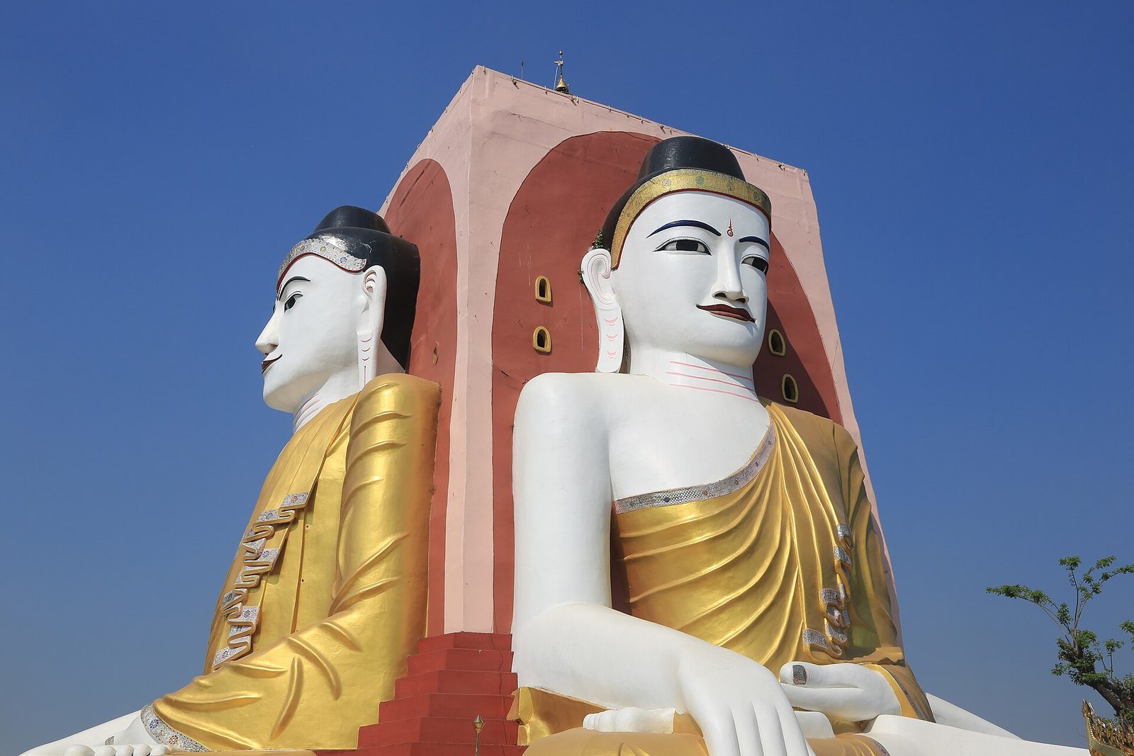 Colossal seated white Buddha figures set back to back against a central pillar.