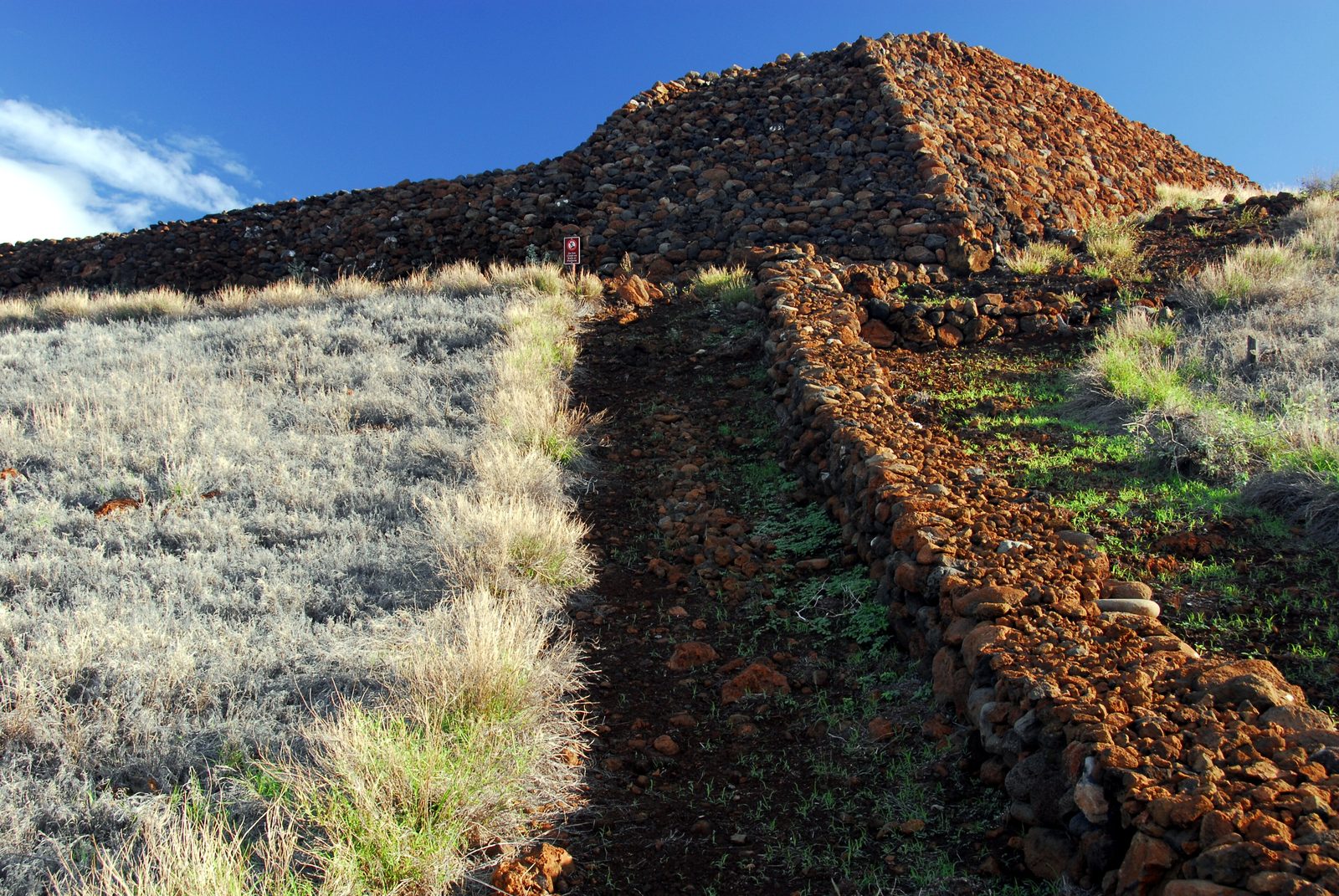 A massive terraced platform of dark stacked stones on a grassy hillside.