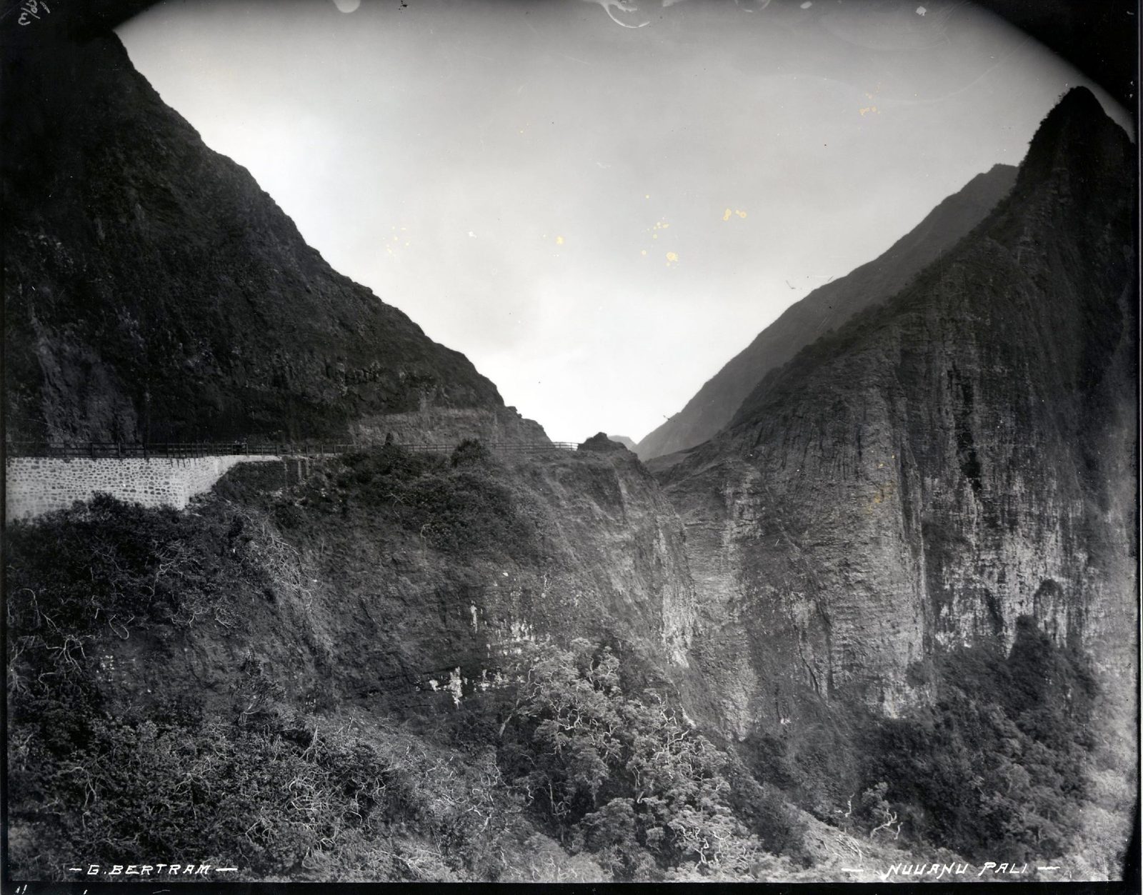 An old photograph of a narrow gap between steep mountain cliffs, a road cut along one side.