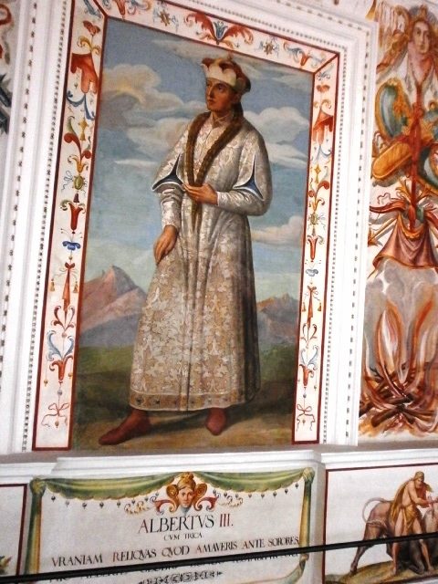 A wall painting of a duke in a long patterned gown standing in a painted niche with a Latin caption.