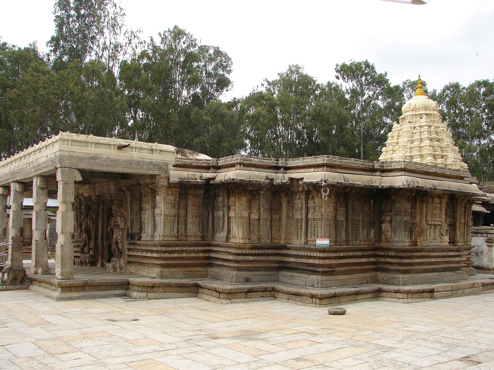 A low stone temple with a pillared hall and a white spire among trees.