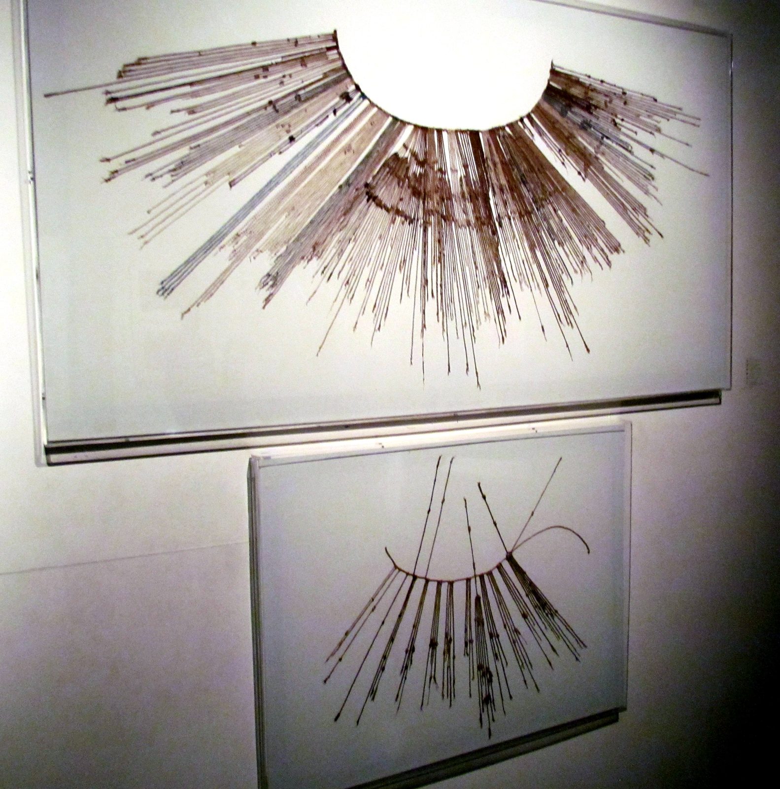 Two quipus, fans of knotted cords hanging from a main cord, mounted on display boards.