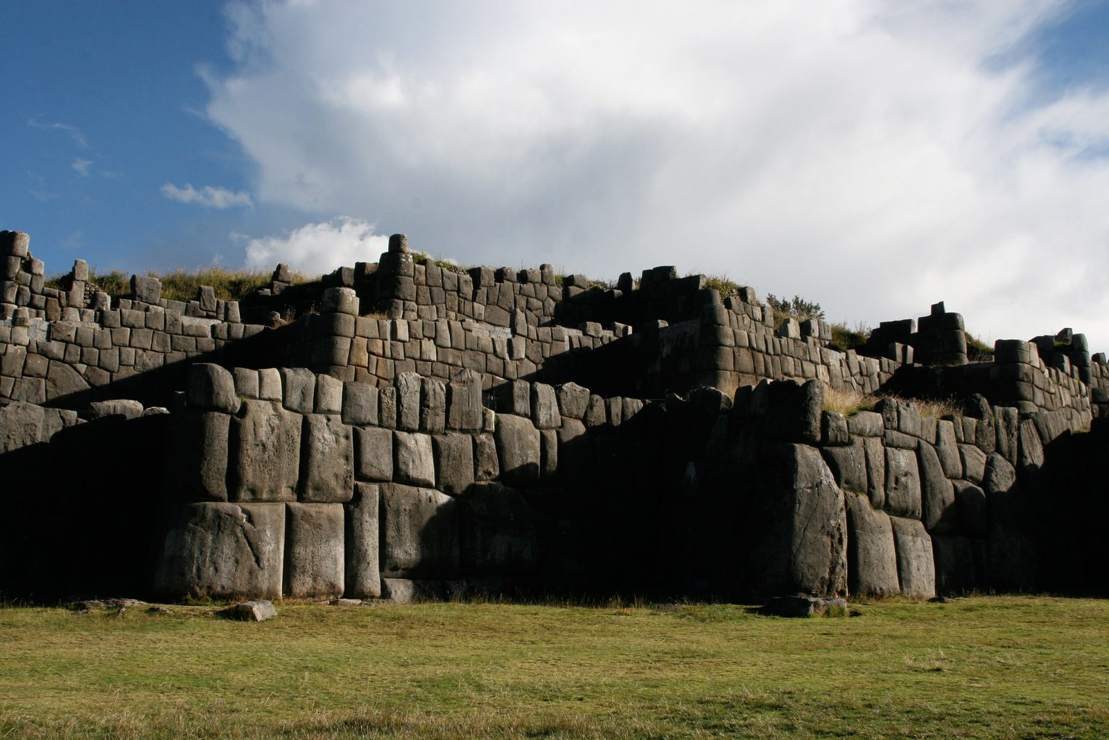 Massive fitted stone walls rising in tiers above a grass field.