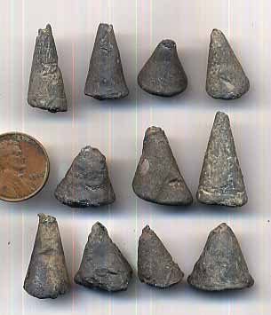 Nine small cone-shaped ingots of dull grey metal arranged in rows on a white ground, pitted and uneven on their surfaces, with a coin beside them for scale.