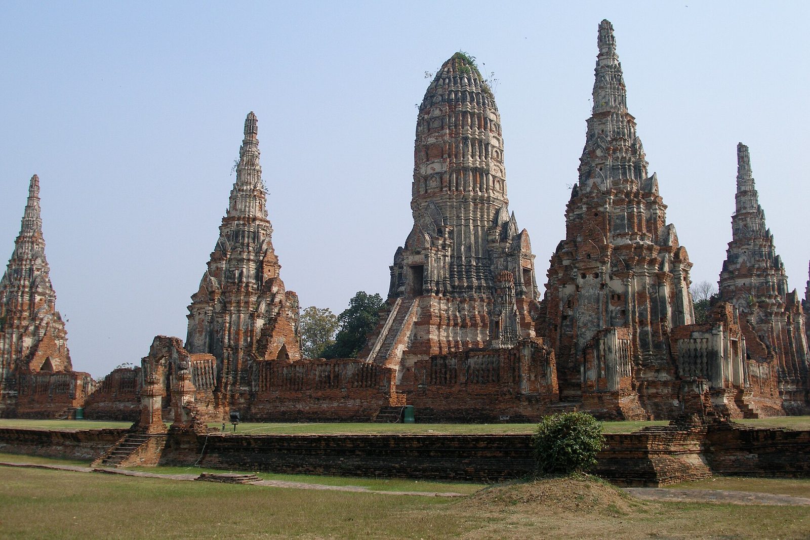 Ruined brick towers of a temple complex standing on a lawn under a clear sky.