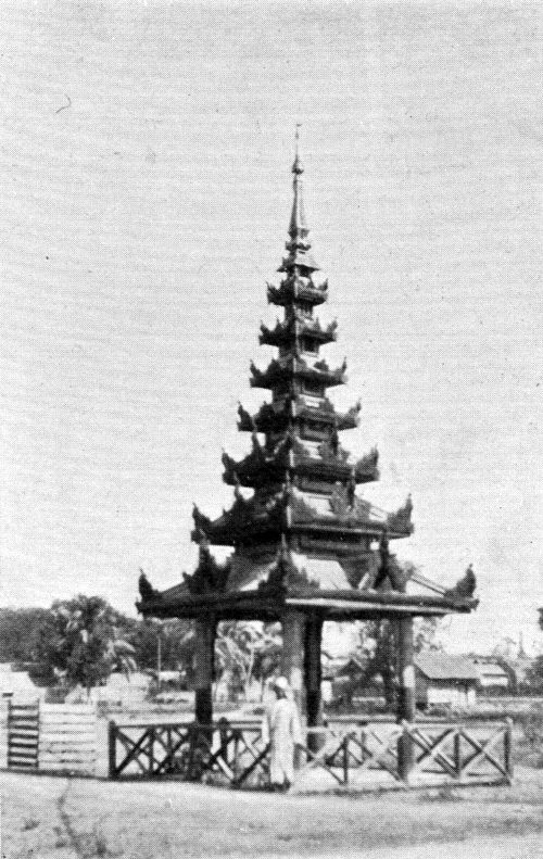 An old photograph of a tall tiered spire over a tomb, inside a fence.