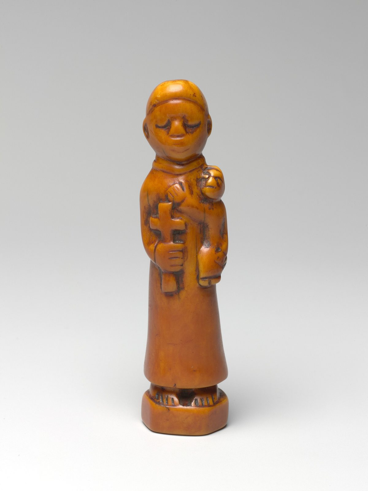 A small ivory figure of a monk holding a cross in one hand and a child on his arm.
