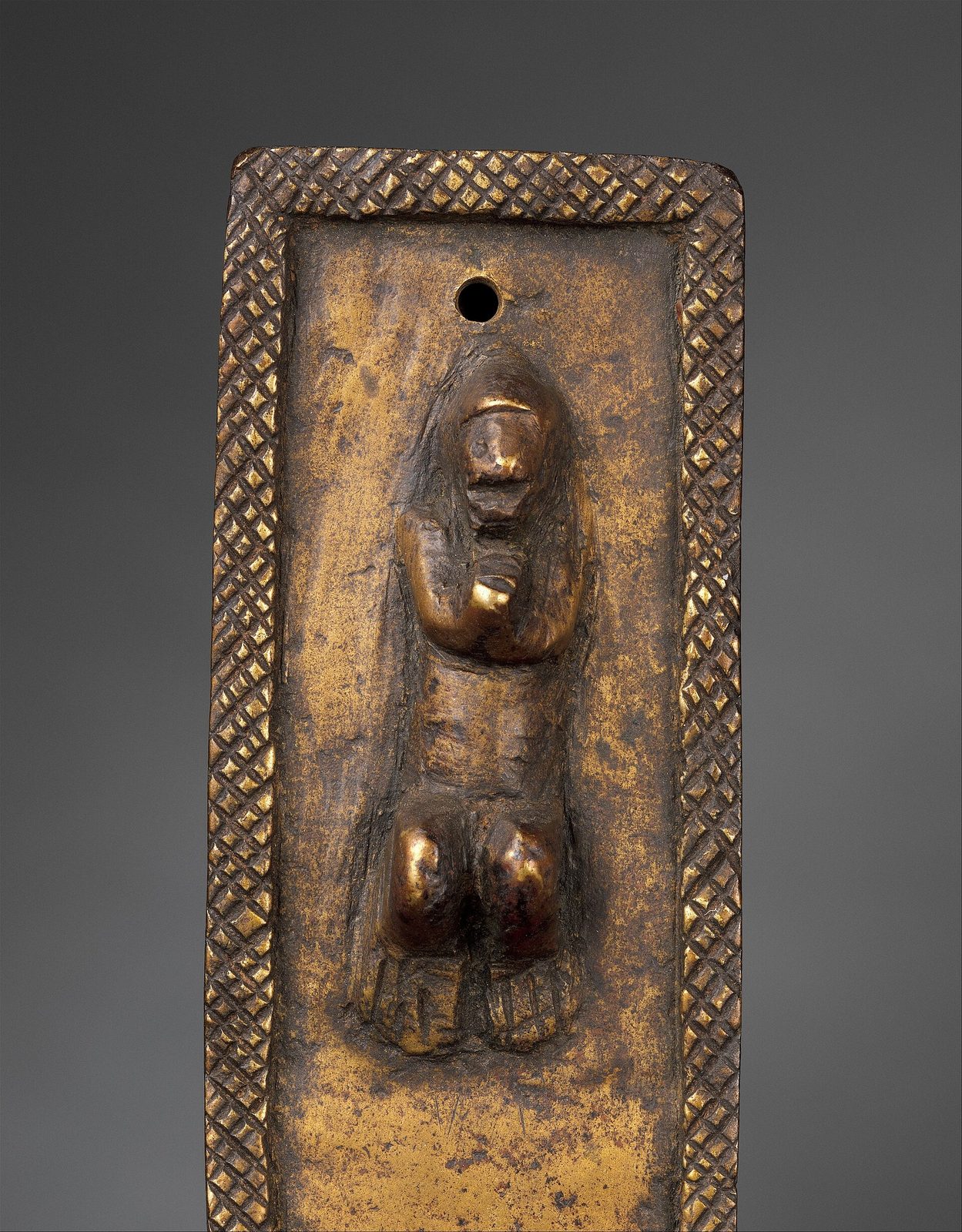 A close view of a small cast brass figure of Christ on a cross with a cross-hatched border.