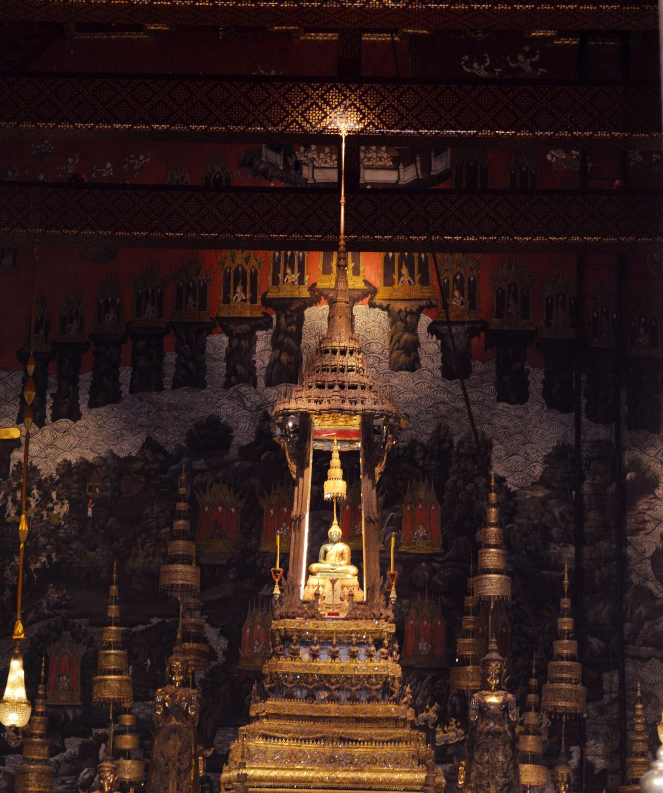 A small green Buddha on a towering gilded altar in a dim hall.