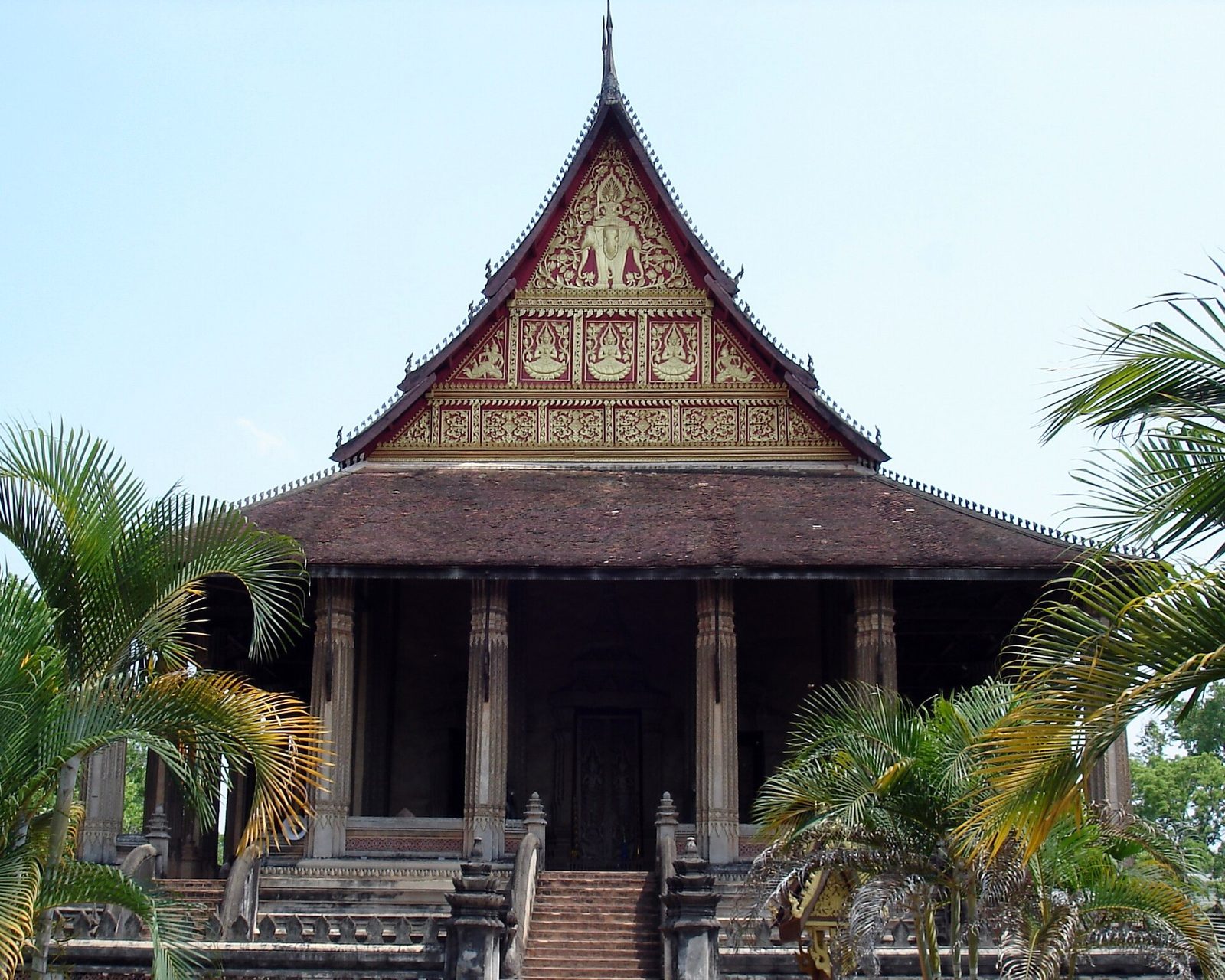 A temple with a steep roof on a stepped platform among palms.
