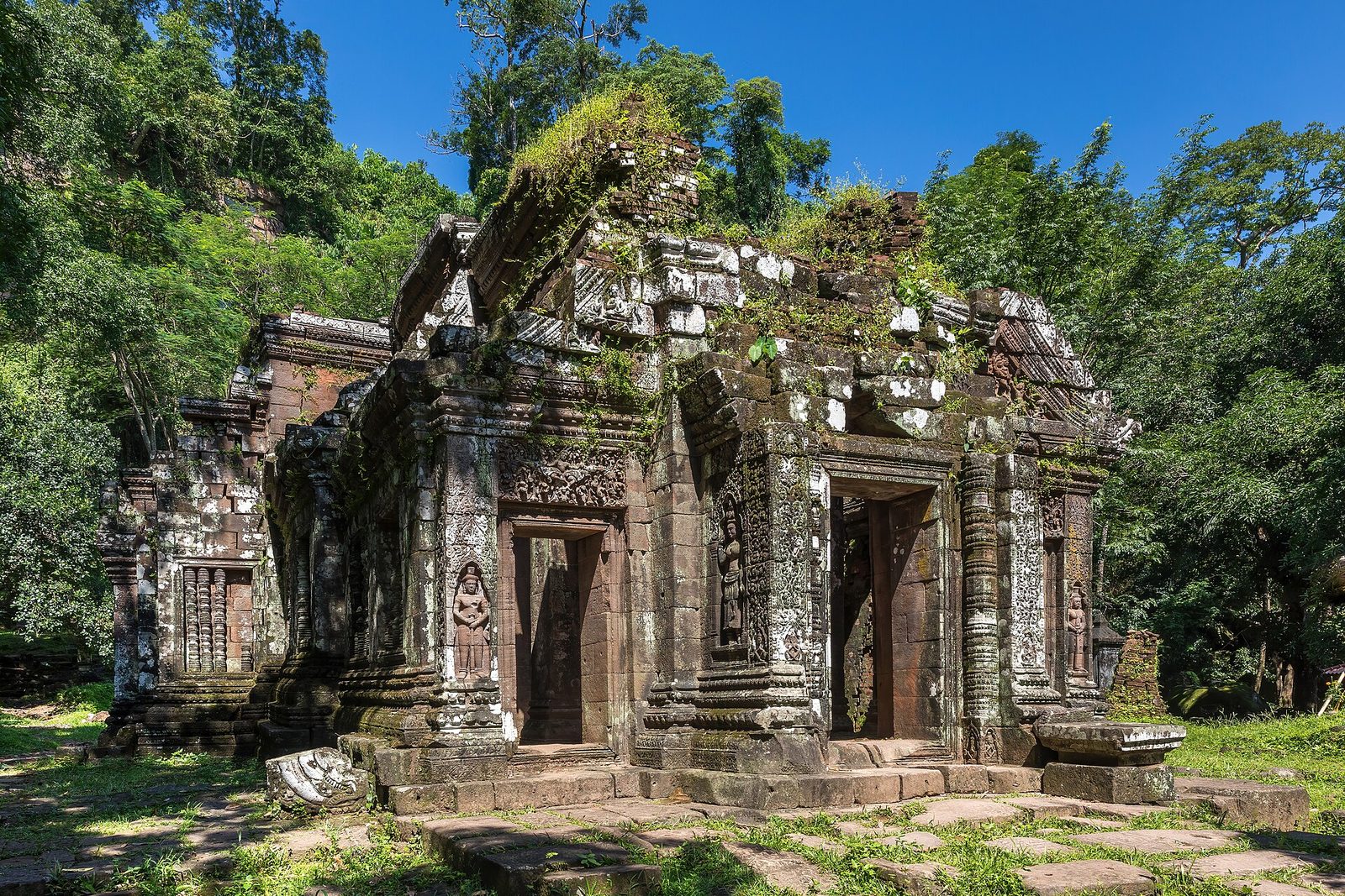 A ruined Khmer stone temple among trees on a hillside.