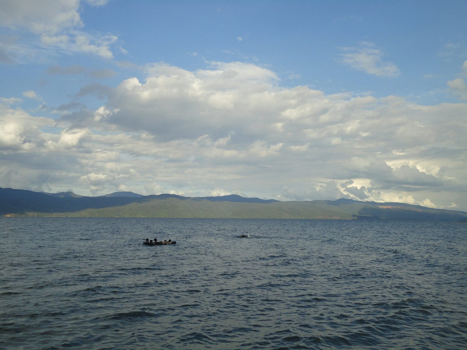 A broad lake under a sky of white cloud, a small boat on the water and low mountains along the far shore.