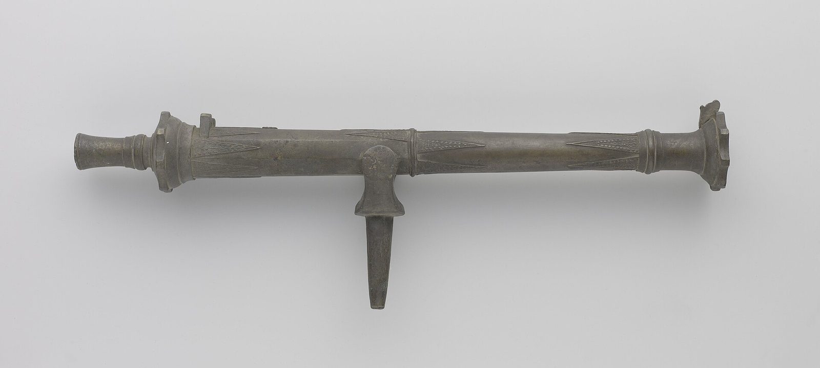 A bronze swivel gun with a long barrel and a pivot pin, photographed on a plain grey ground.