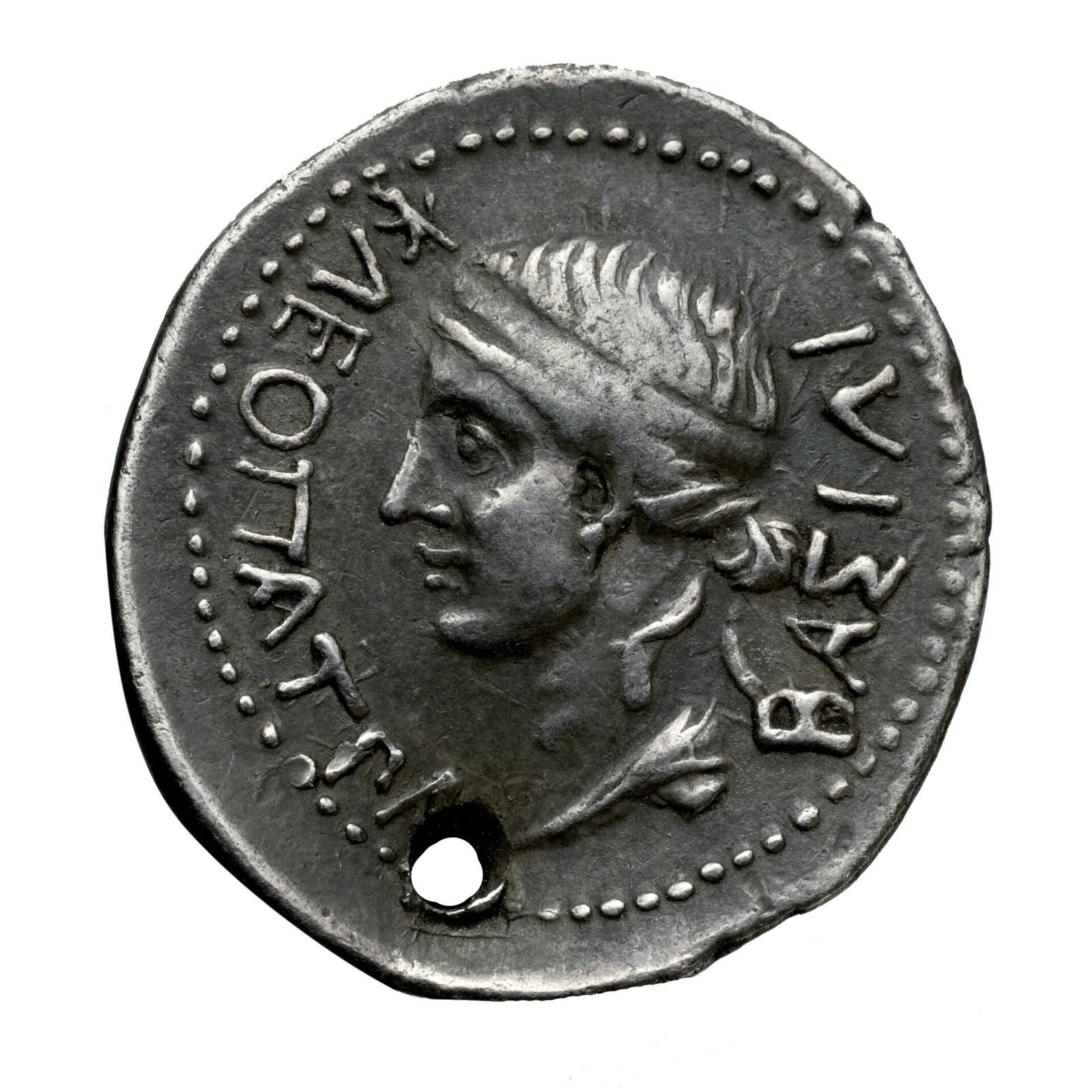A worn silver coin with a woman's head in profile and a Greek legend.