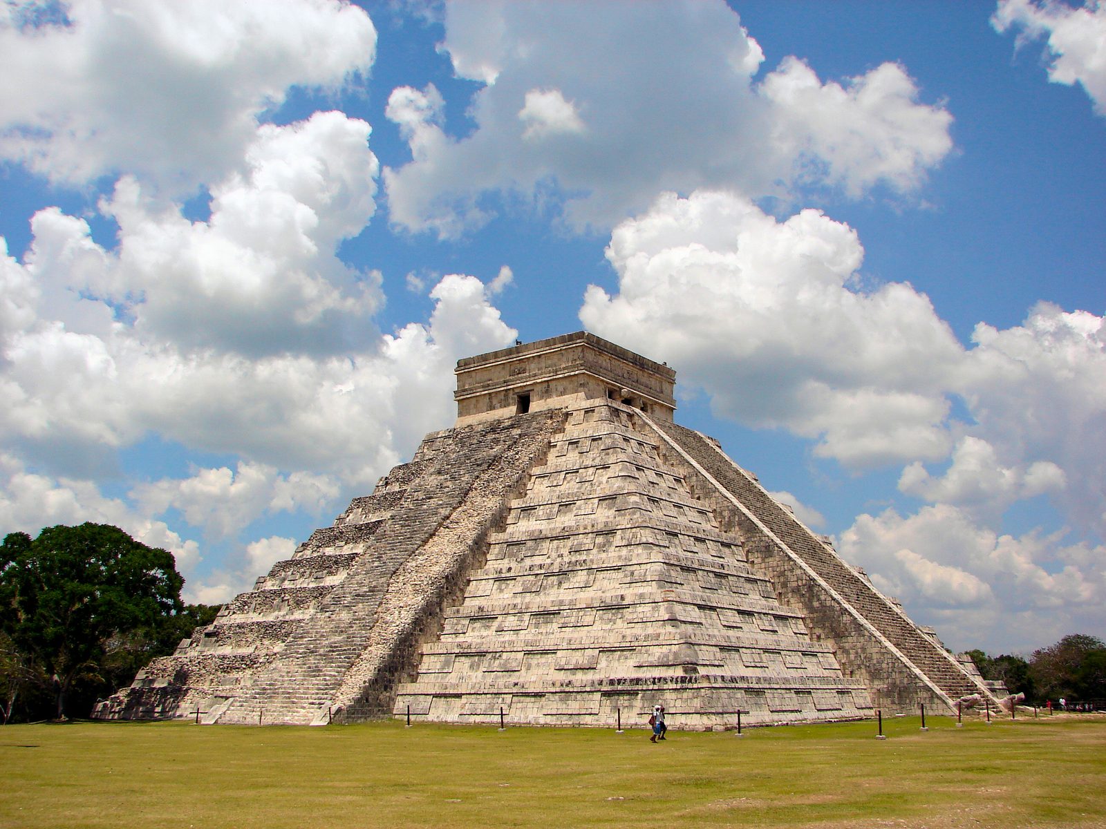 A tall stepped pyramid with stairs on two faces and a temple on top, under a cloudy blue sky.
