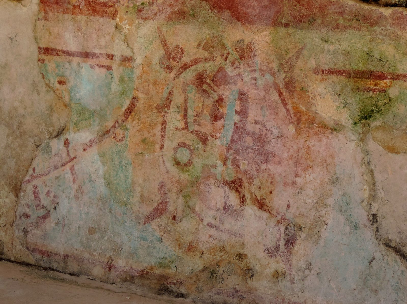 Faded red, green and ochre wall painting on a plaster surface.
