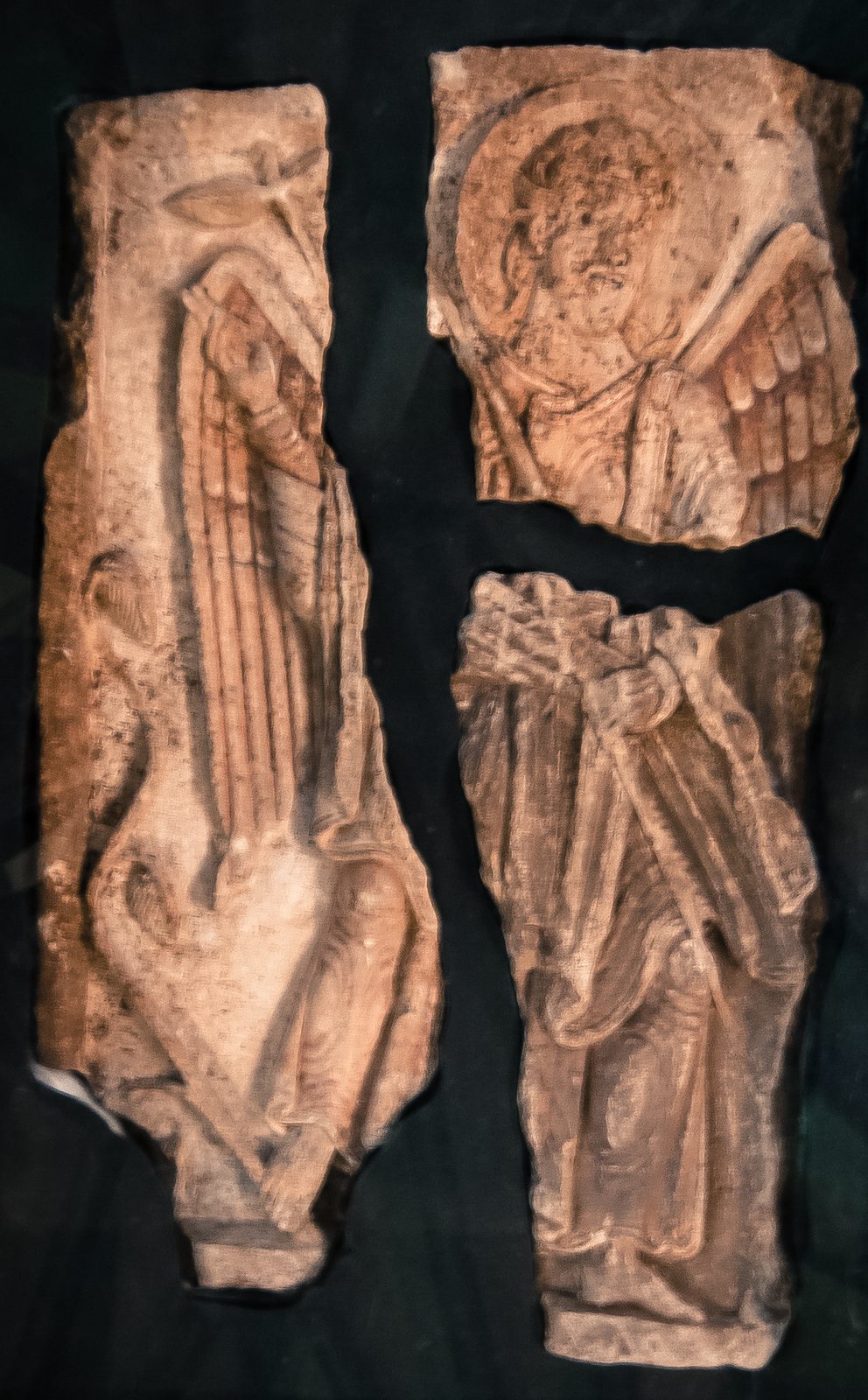 Three fragments of a carved limestone panel showing a standing angel with spread wings.