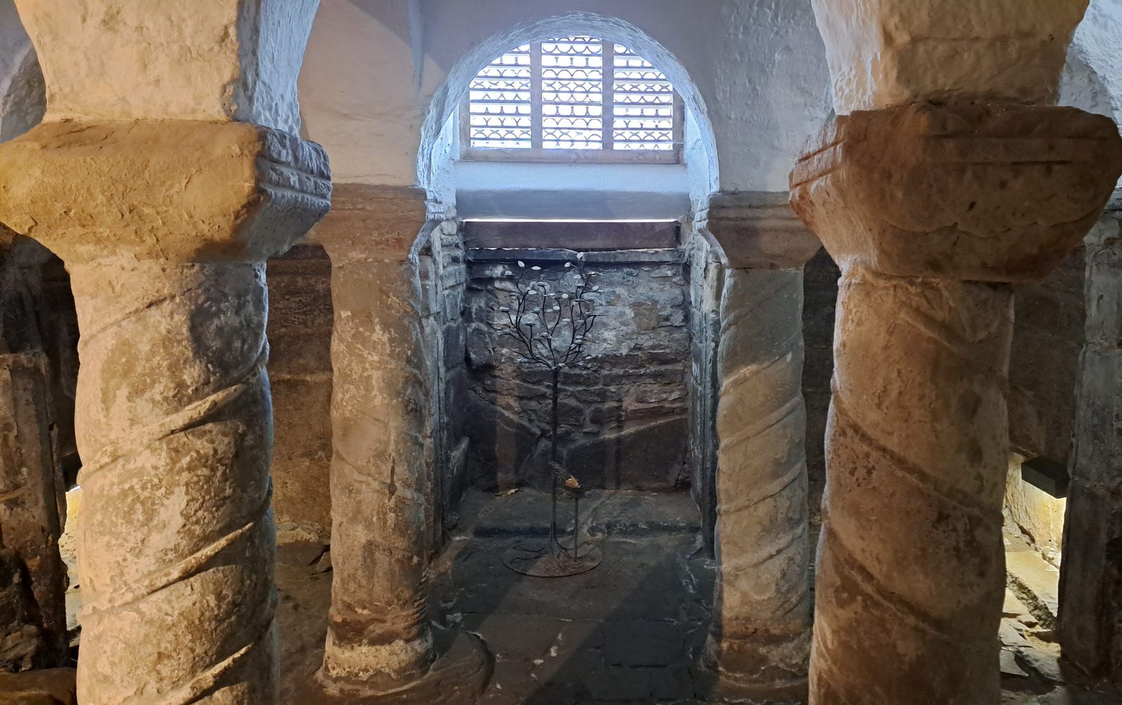 A low vaulted crypt with spirally carved stone columns, lit from a small window.