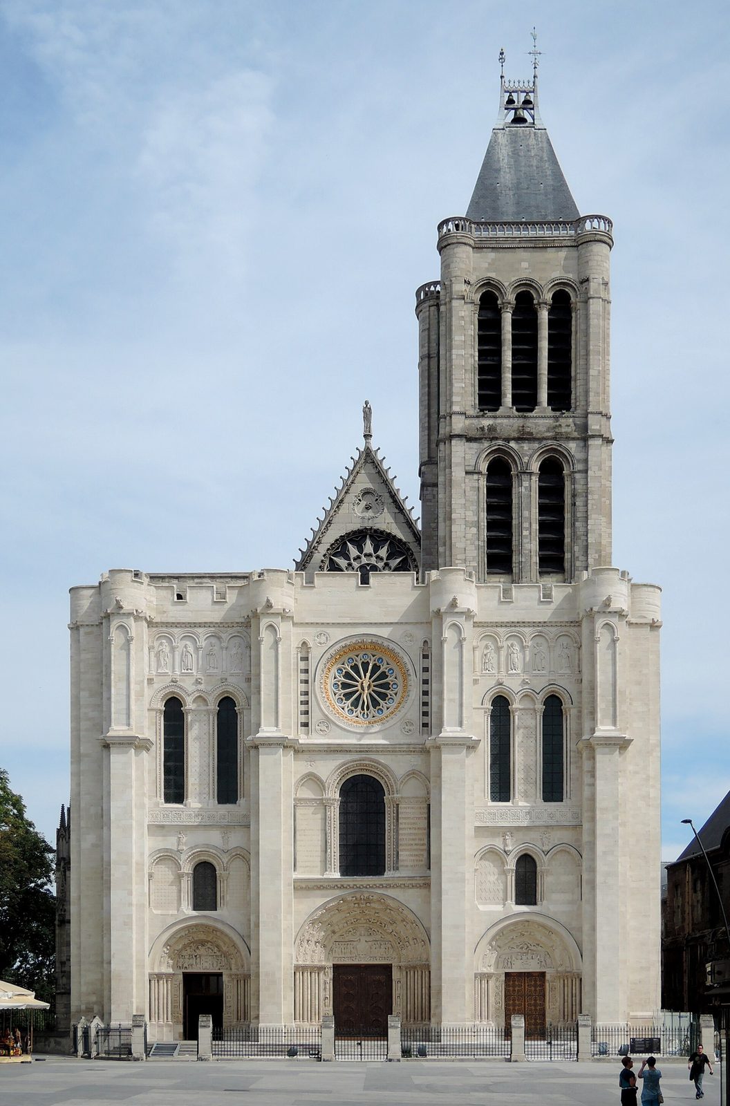 The west front of a large Gothic church with a single surviving tower, a rose window above three deep carved portals.
