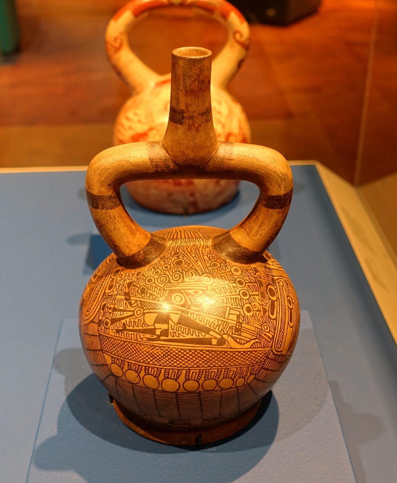 A cream ceramic stirrup-spout bottle painted in fine red line with boats and sea creatures.