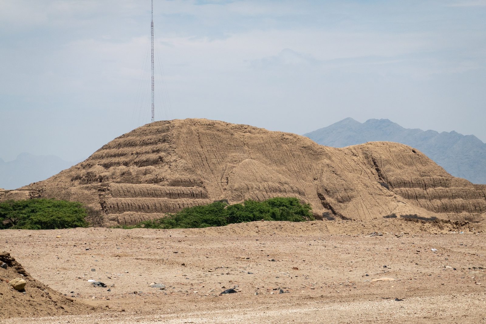 A huge eroded mud-brick platform with ridged flanks rising from a dry plain, mountains behind.