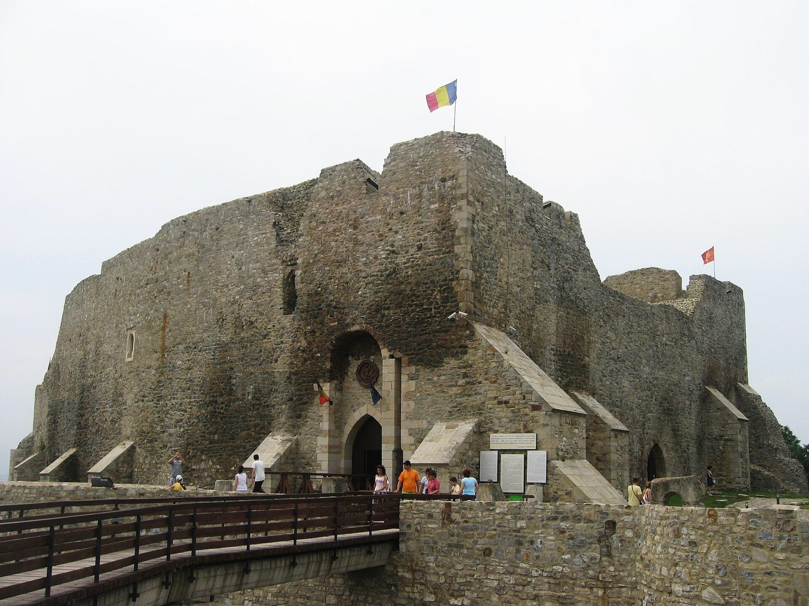 A massive stone citadel on a hilltop, reached by a long wooden bridge.