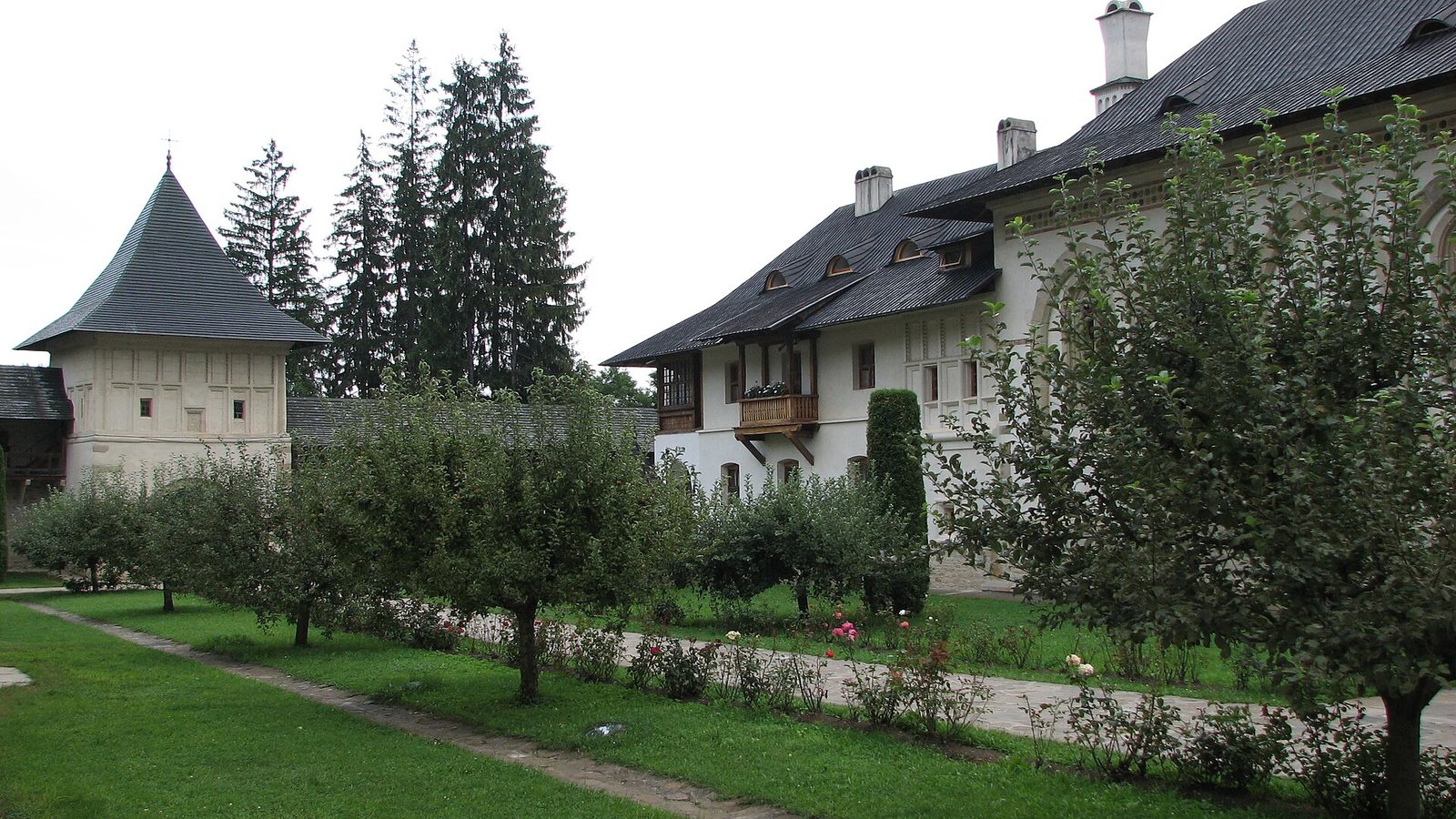 A monastery courtyard with a white-walled tower and residence among fruit trees.