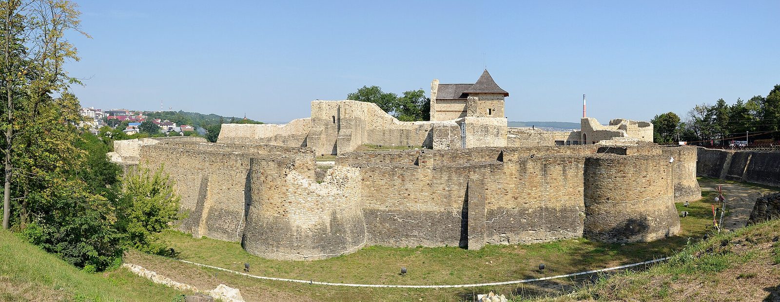 A wide view of the ruined walls and towers of a large stone fortress on a grassy rise.