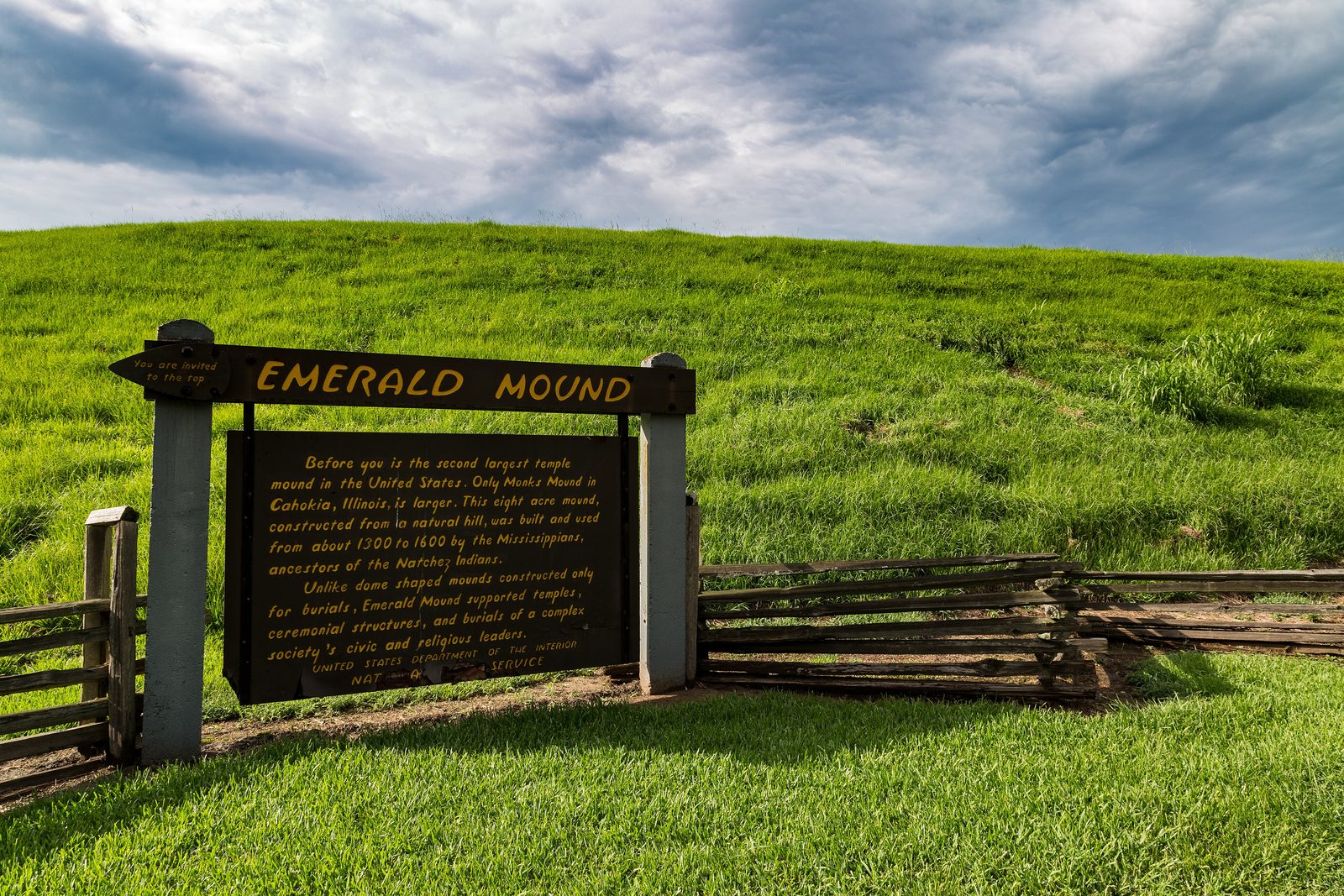 A tall grass-covered mound with a wooden sign at its foot.