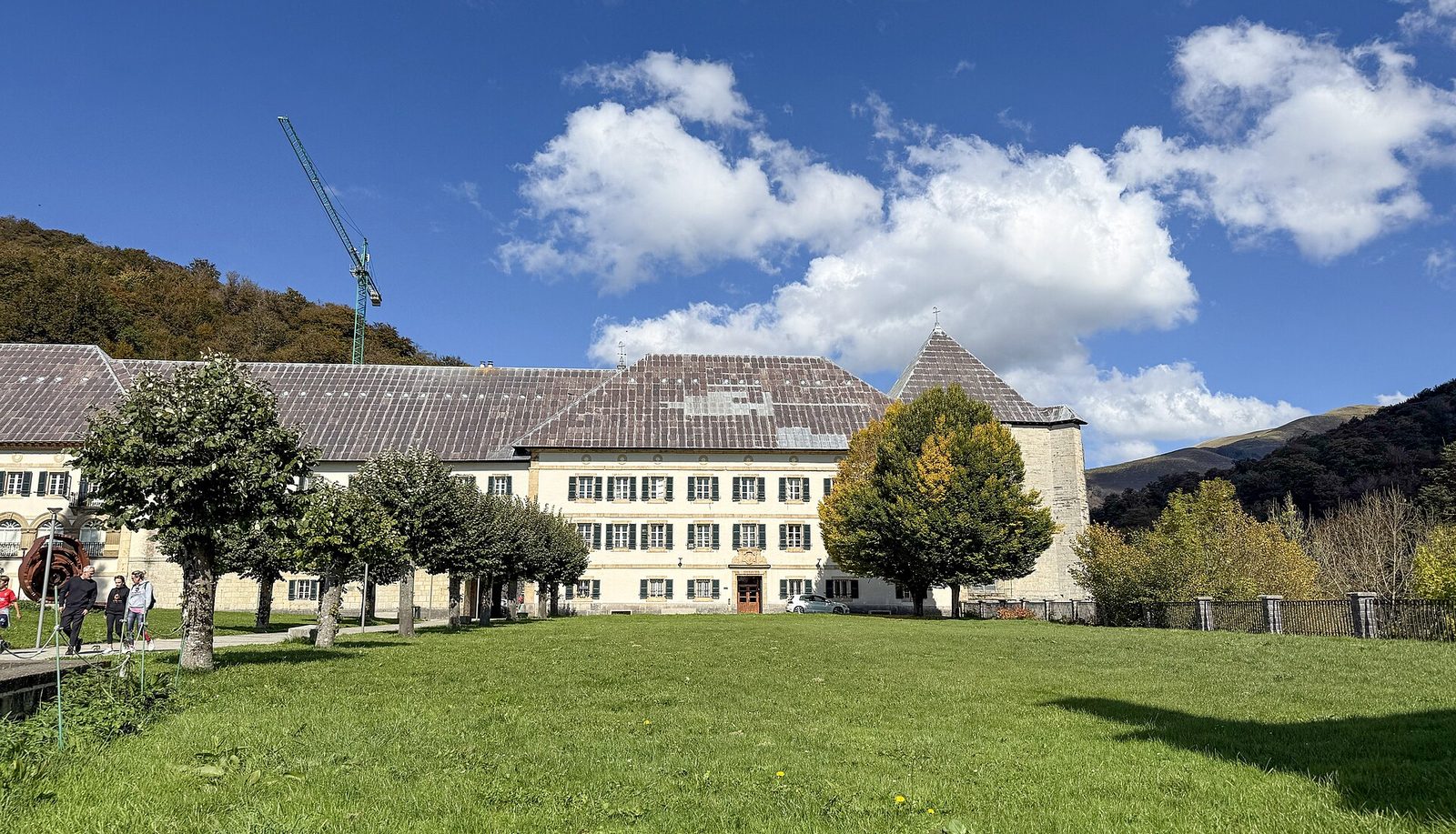 A long stone church and conventual buildings in a green mountain valley under a blue sky.