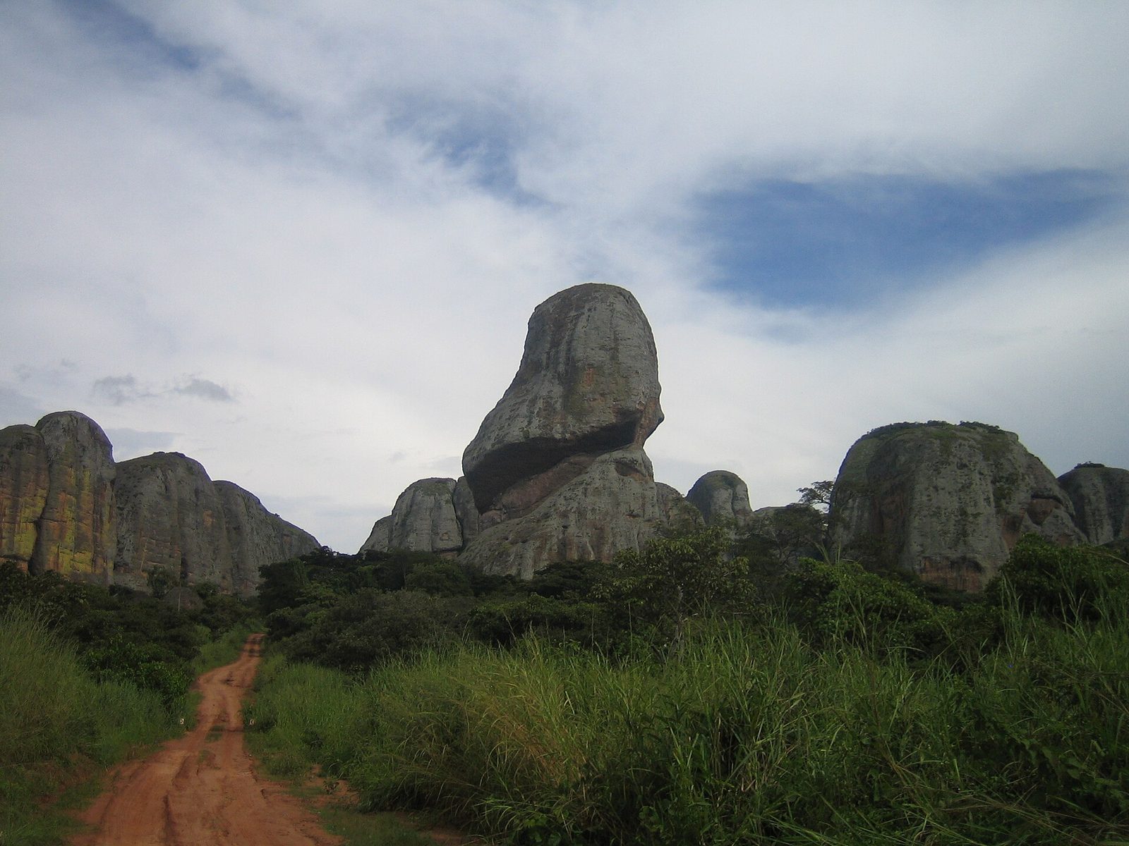 Huge rounded black rock formations rising above green bush, a dirt track leading towards them.