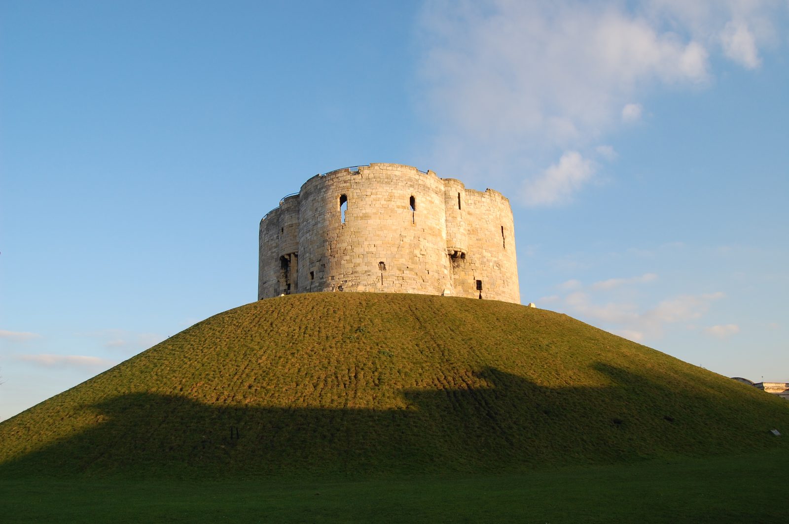 A round stone keep on top of a steep grassy mound.