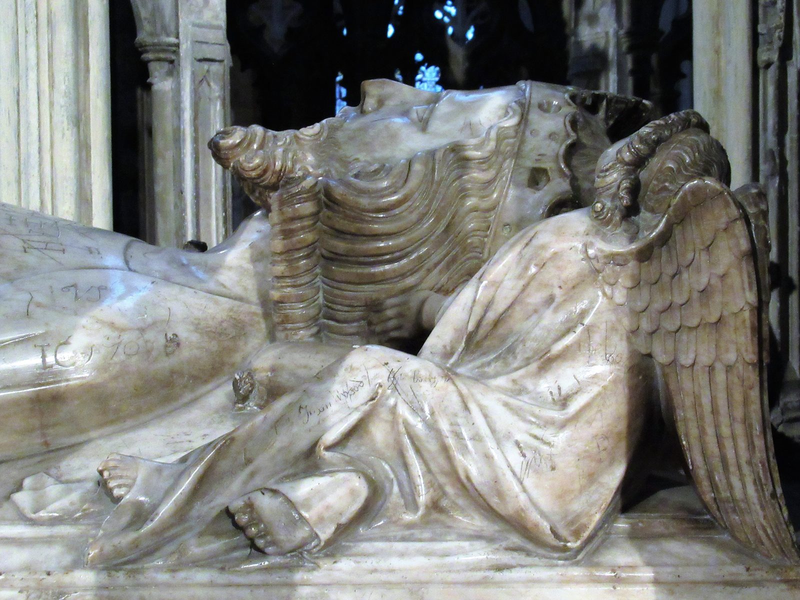 A white alabaster effigy of a crowned king with angels at his head, under a carved canopy.