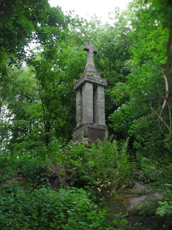 A stone monument topped by a cross, half hidden among trees.