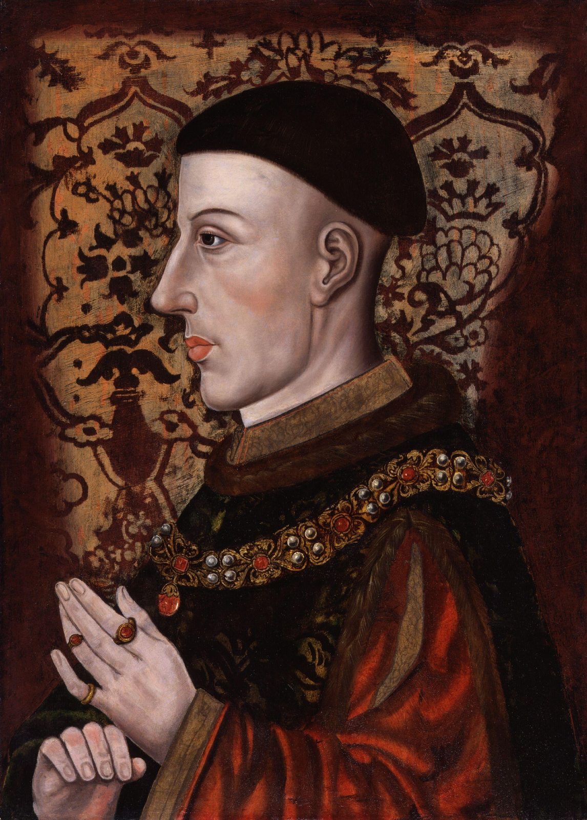 A profile portrait of a man with a cropped haircut in a red gown, his hands together.