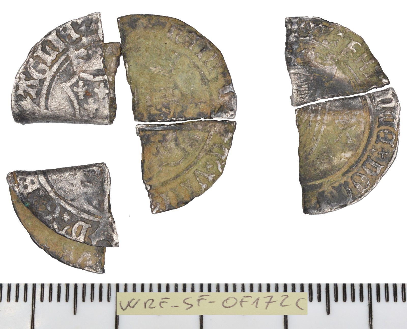 A broken silver coin in four pieces beside a millimetre scale.