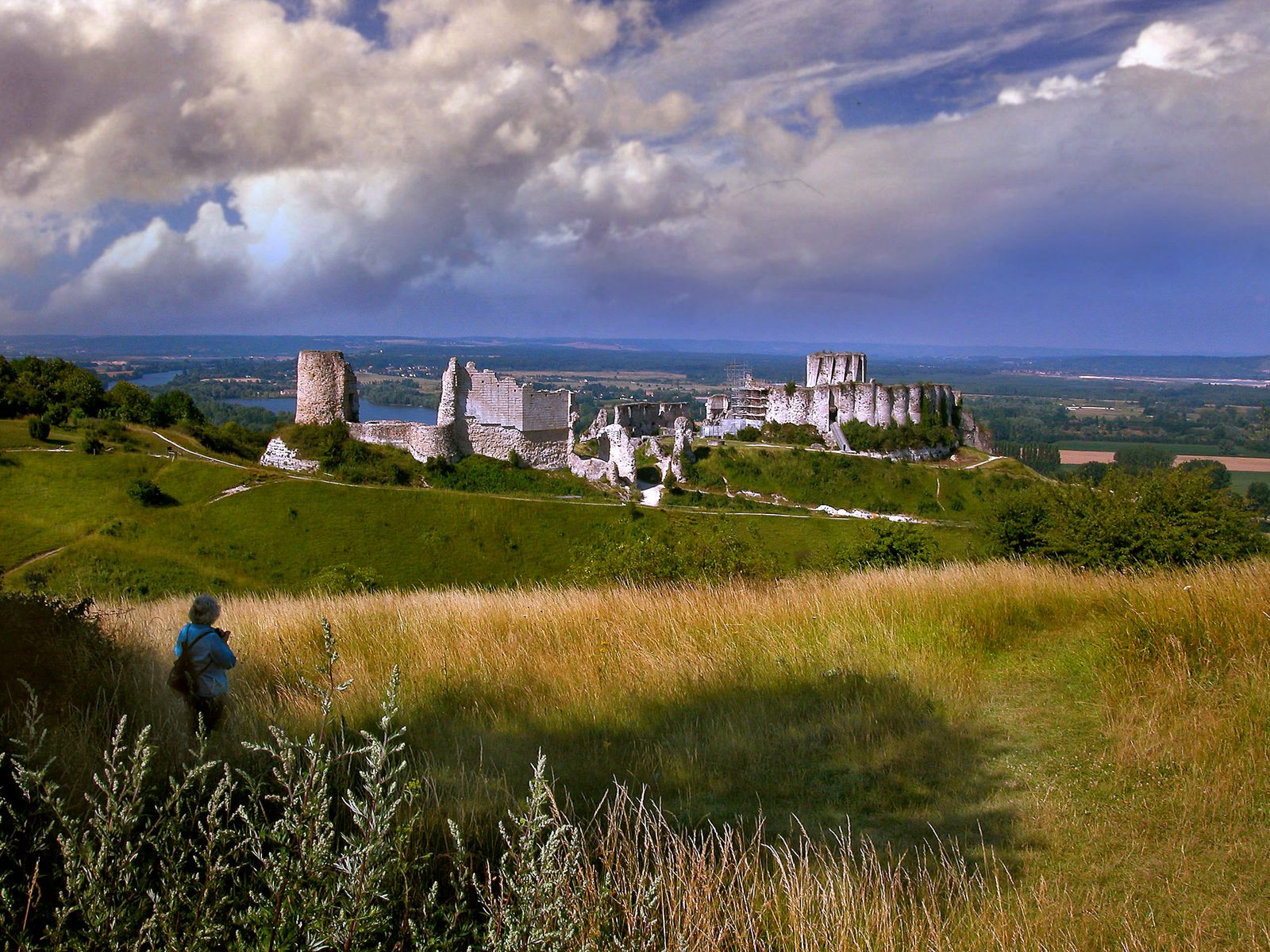 Castle ruins on a chalk ridge above a broad river valley, seen across a grassy slope.