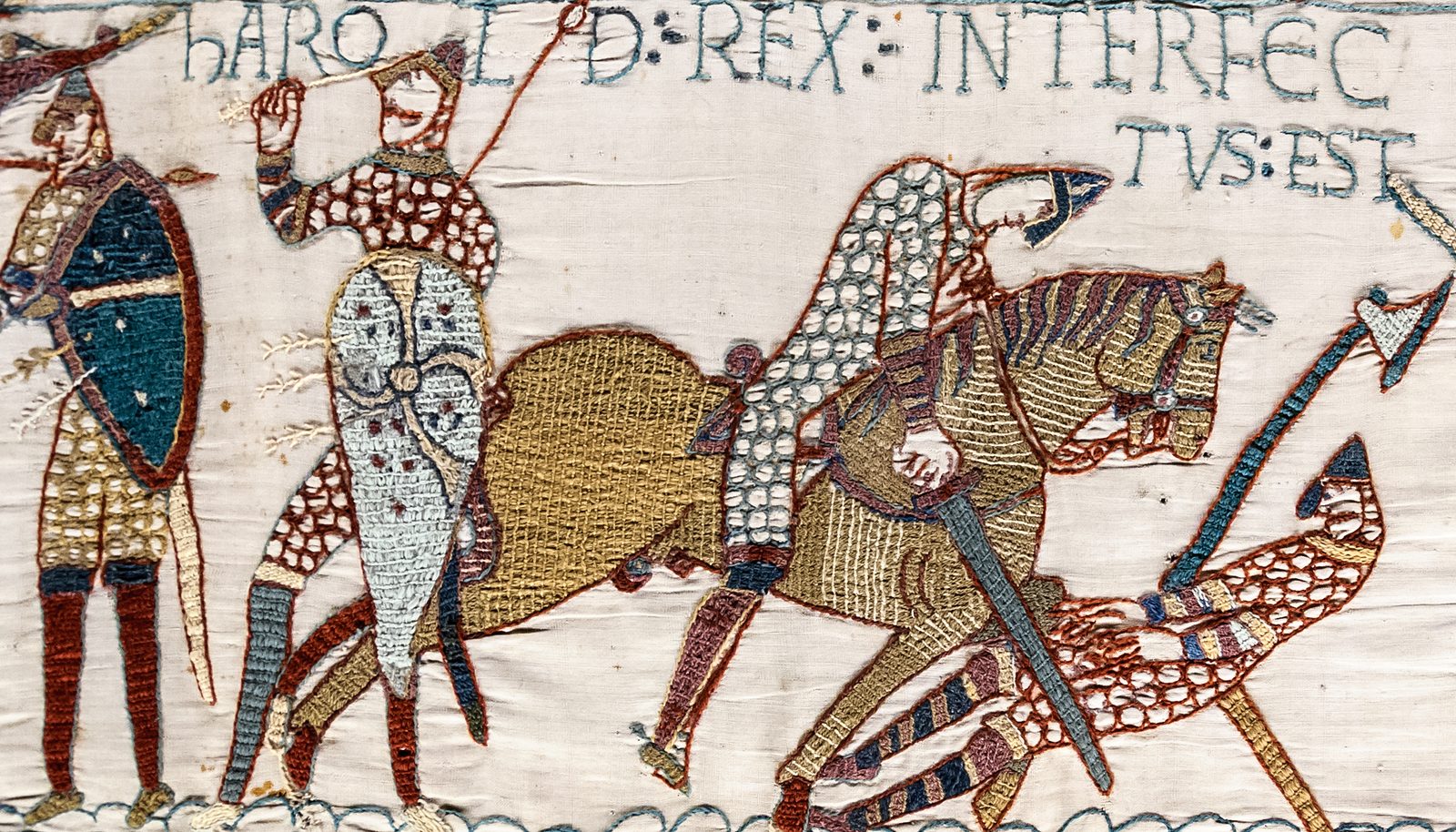 An embroidered strip of mounted knights and a falling warrior beneath the words HAROLD REX INTERFECTUS EST.