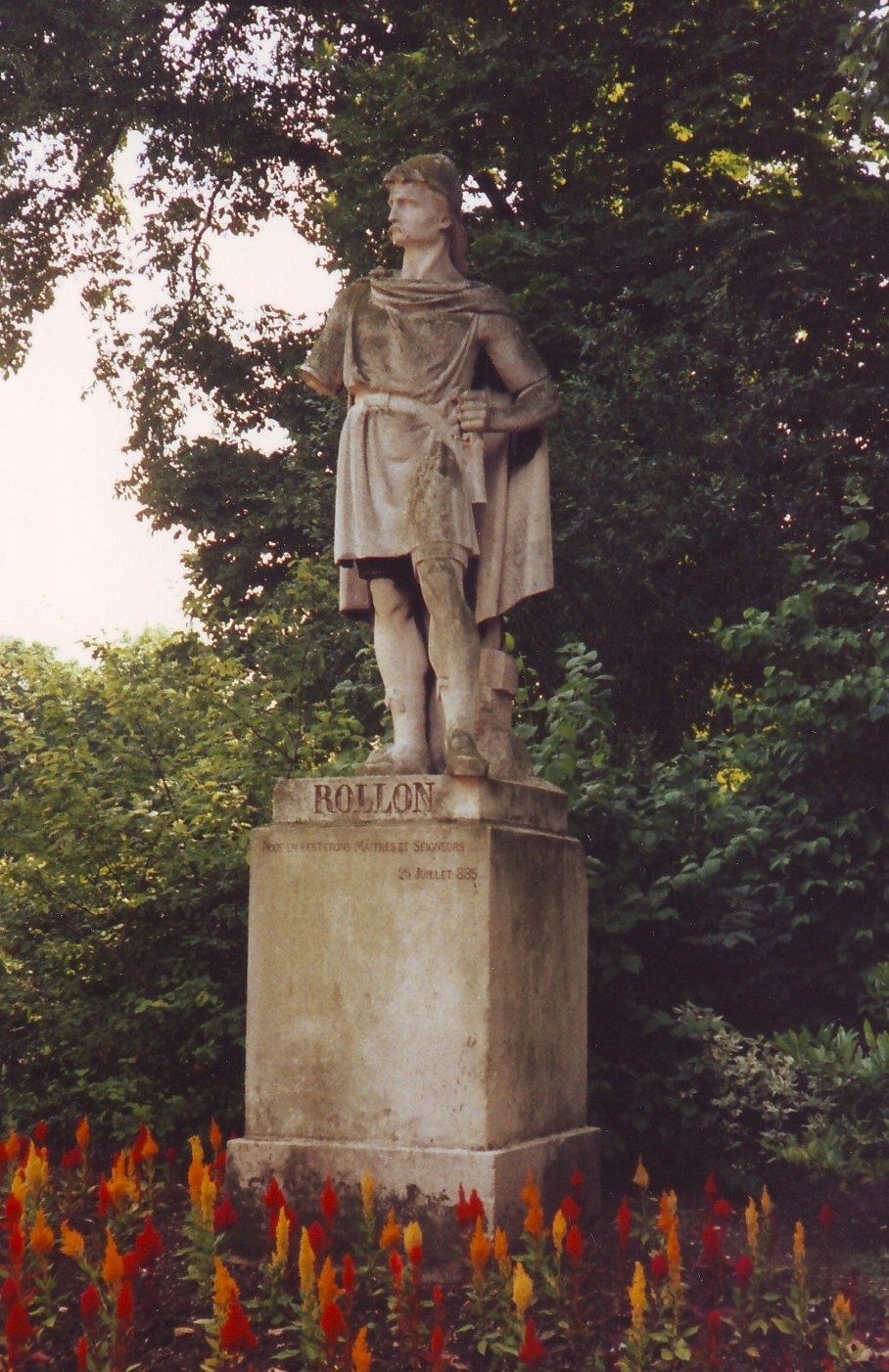 A stone statue of a cloaked warrior on a pedestal inscribed ROLLON, in a park.