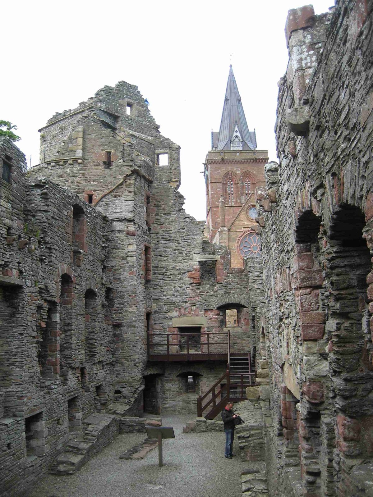 The roofless ruins of a stone palace, with the red sandstone spire of a cathedral rising behind.