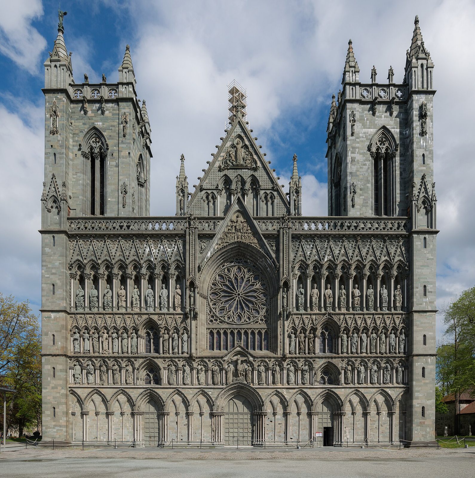 The grey stone west front of a Gothic cathedral with two square towers, a rose window and rows of carved standing figures.