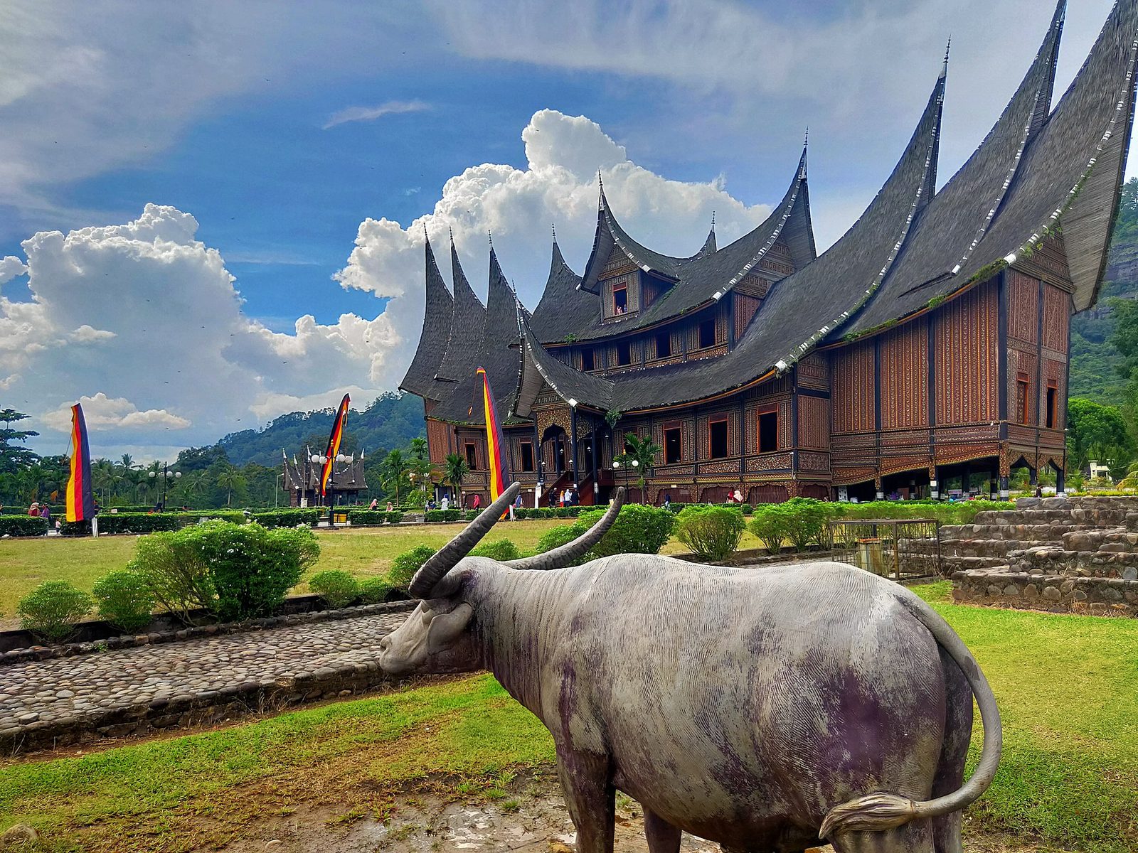 A long timber building raised on posts, its roof rising into a row of sharp upswept gables like horns, painted and carved along the front, with a buffalo statue on the lawn in the foreground.