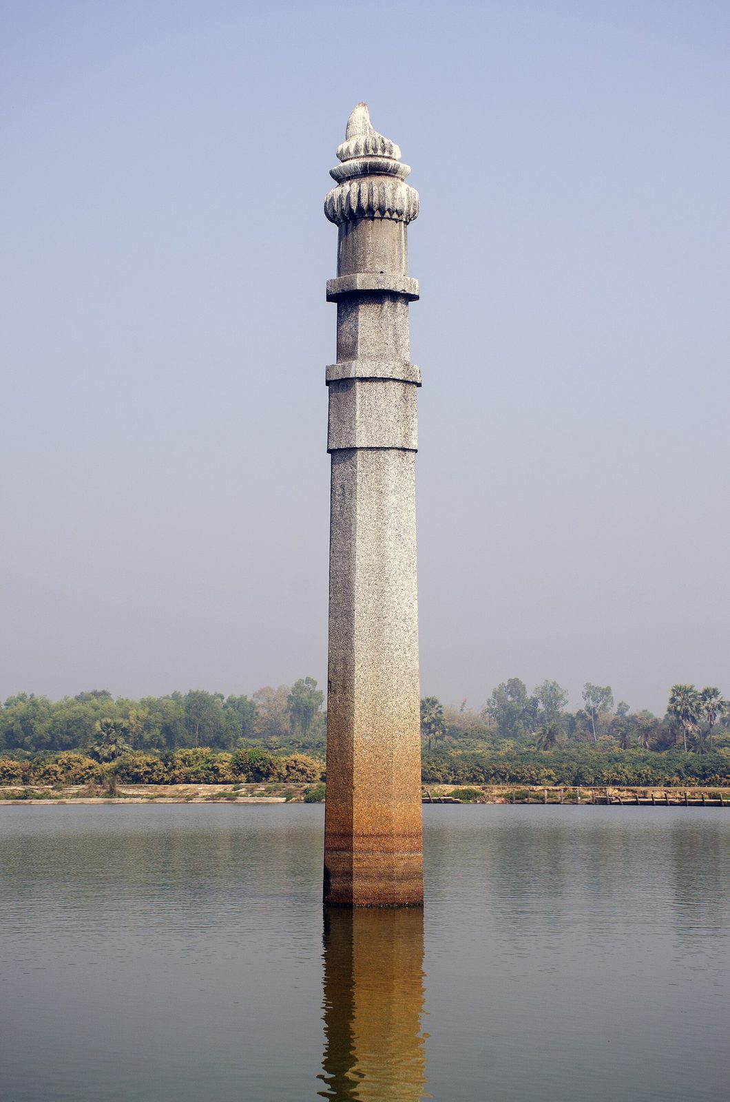 A tall octagonal stone pillar rising out of the water of a large tank.