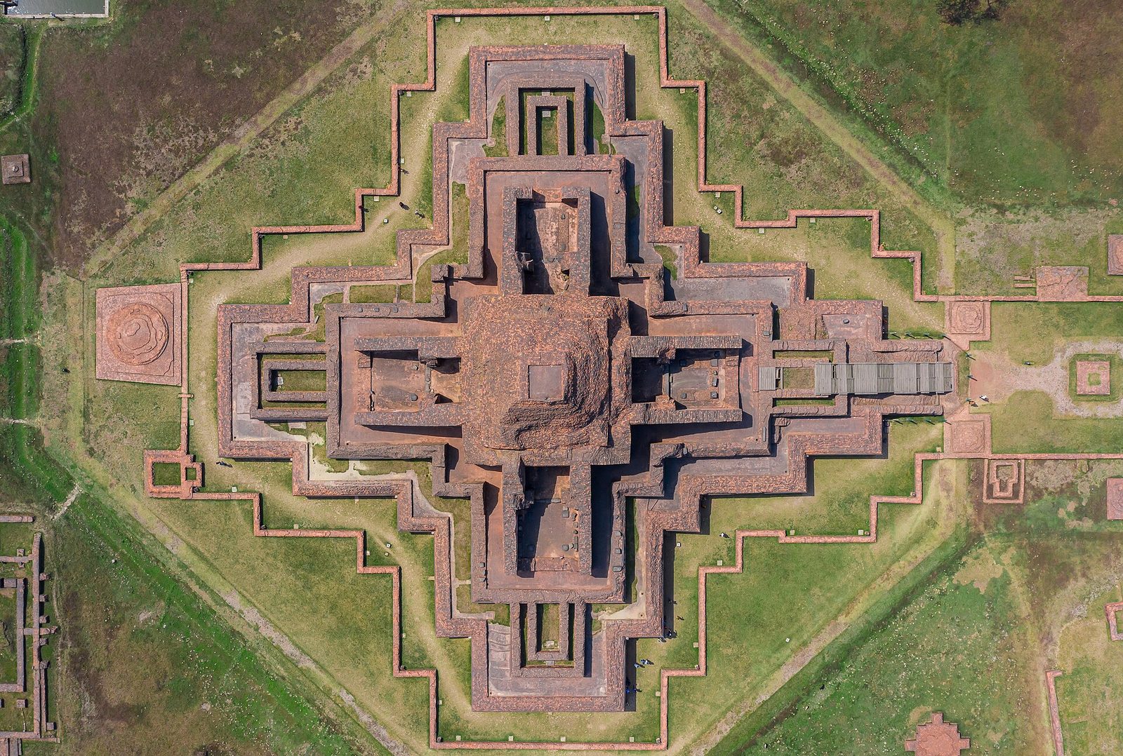 An aerial view of a vast cross-shaped brick temple at the centre of a square courtyard.