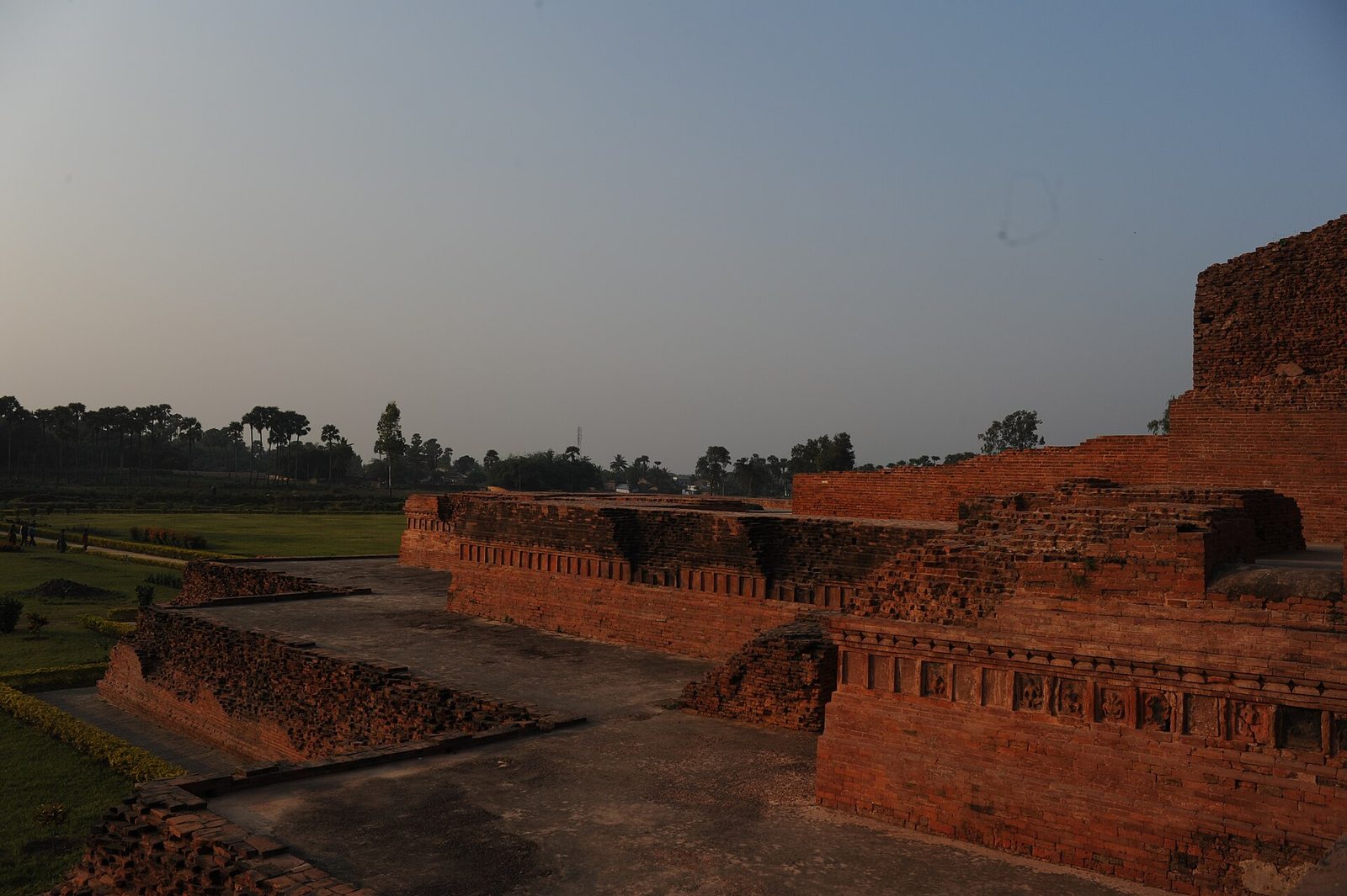 Excavated red-brick terraces of a large monastery at dusk.