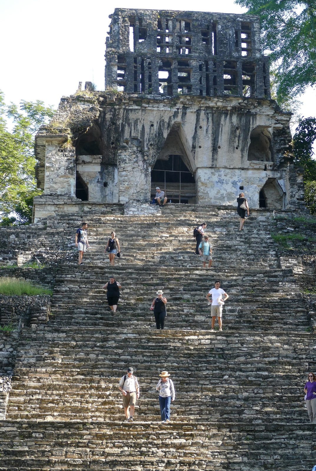 A steep stair climbing to a ruined temple topped by a latticed roof comb, visitors on the steps.